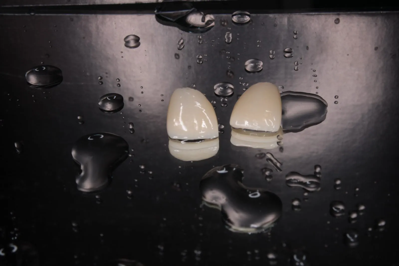 Dos carillas de cerámica con gotas de agua sobre fondo negro